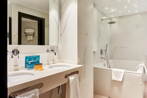 a white bathroom with a sink and a tub at Silken Ciudad Gijón in Gijón