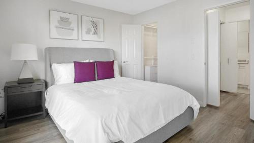 a white bedroom with a large bed with purple pillows at Landing Modern Apartment with Amazing Amenities (ID1233X125) in Redlands