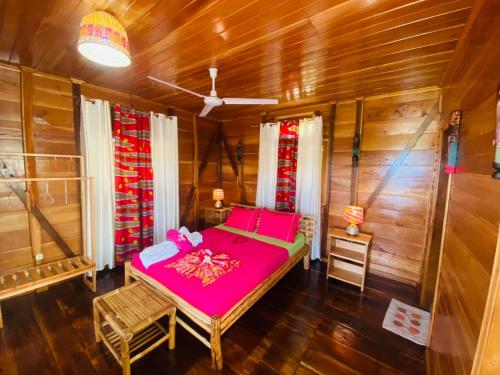 a bedroom with a pink bed and wooden walls at Monte Mar SãoTomé in M. Peixe