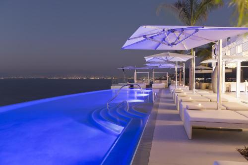 a swimming pool with lounge chairs and umbrellas at night at Hotel Mousai - Adults Only in Puerto Vallarta