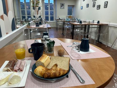 a table with a plate of food and bread and orange juice at Cit'Hotel le Challonge in Dinan