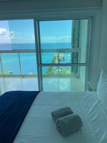 een wit bed met een handdoek voor een raam bij Ap com vista mar - Cloc Marina! in Salvador