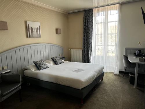 a bedroom with a bed and a desk and a window at Cit'Hotel le Challonge in Dinan