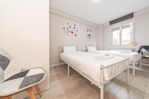 a white bedroom with two beds and a chair at Elegant 6 pax apartment in Plaza Eliptica - SM17 in Madrid