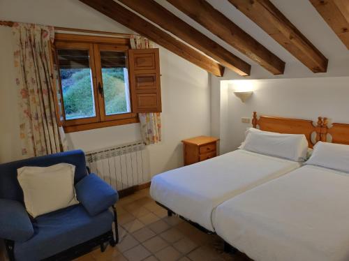a bedroom with two beds and a blue chair at Hostal Posada La Panadera in Sepúlveda