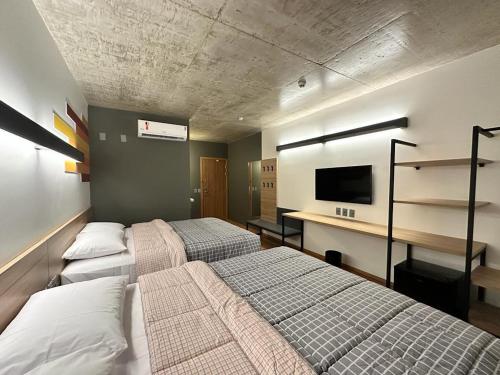 a bedroom with two beds and a desk with a tv at Hotel 10 Sorriso in Sorriso
