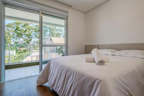 Cama blanca en habitación con ventana grande en Belo apto com varanda a 150m do mar ABC202, en Itajaí
