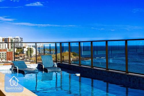 einen Pool mit zwei Stühlen und das Meer in der Unterkunft Apartamento aconchegante na Barra com vista mar in Salvador
