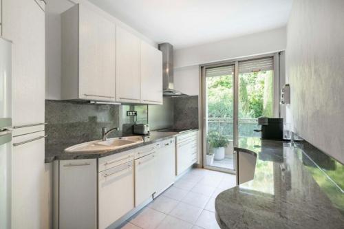 une cuisine avec des placards blancs et une grande fenêtre dans l'établissement Bright one-bedroom in a quiet area wswimming pool, à Cannes