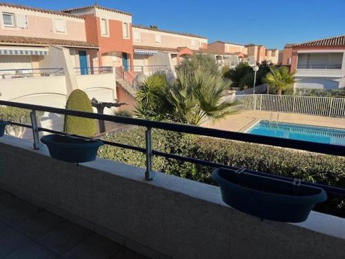 - un balcon avec 2 casseroles sur une balustrade et une piscine dans l'établissement Appartement T2 avec Terrasse, Parking Privé et Piscine Sécurisée, Proche Plage Richelieu - FR-1-749-37, au Cap d'Agde