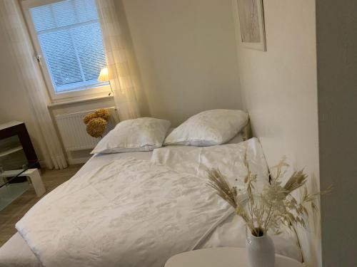 a bed with white sheets and a vase on a table at Ferienwohnung Schleistübchen in Fahrdorf