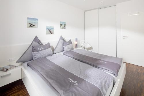 um quarto branco com uma cama com lençóis e almofadas cinzentas em NeysTime em Norderney