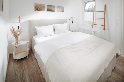 ein weißes Schlafzimmer mit einem großen weißen Bett und einem Fenster in der Unterkunft Haus Salz & Sand Whg Sand in Norderney