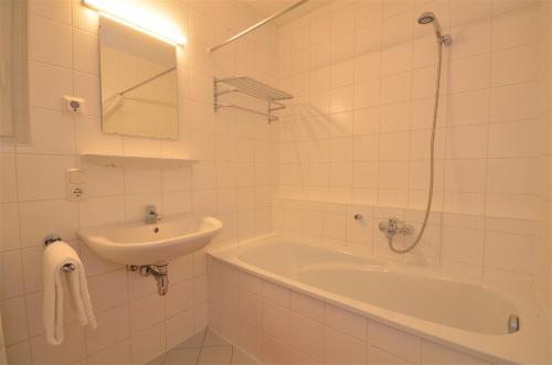 Baño blanco con lavabo, bañera y espejo en Panoramic View - by Alpen Apartments, en Piesendorf