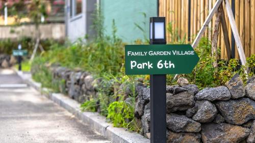 a green street sign in front of a stone wall at Jeju Family Garden Village in Jeju