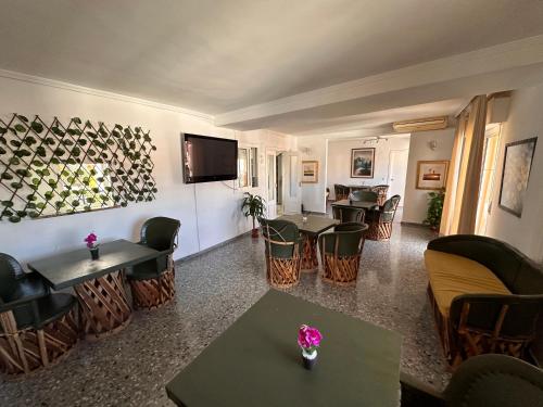 una sala de estar con mesas y sillas y TV de pantalla plana. en Hostal San Felipe, en Marbella