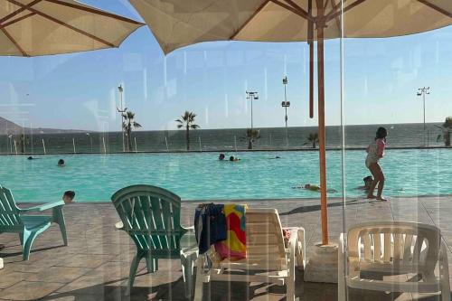 イキケにあるDepto frente a Playa con hermosa vista al mar Condominio Mar Egeoの椅子と傘を置いたスイミングプールの横に立つ女性