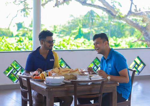 two men sitting at a table with food on it at Birdsong Leisure Resort in Tissamaharama
