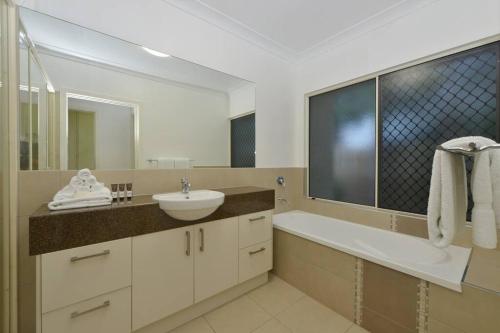 a bathroom with a sink and a tub and a mirror at The Red Anchor in Port Douglas
