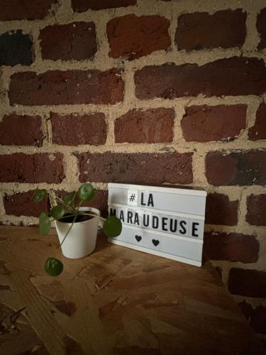a sign in front of a brick wall with a plant at La Maraudeuse in Theux