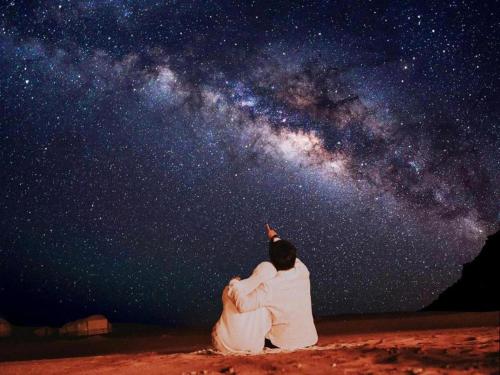 a couple sitting on the ground looking up at the universe at Wadi Rum Desert Tours and Glamping with Hussein in Wadi Rum
