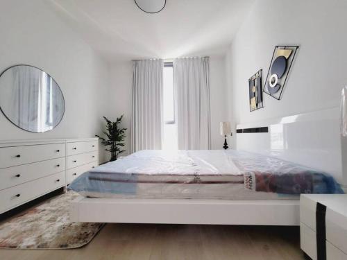 a white bedroom with a large bed and a mirror at Luxury cozy apartment Al jda in Sharjah