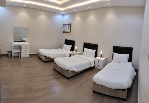 3 camas num quarto com paredes brancas e pisos em madeira em فلل الكناري الراقية em Taif