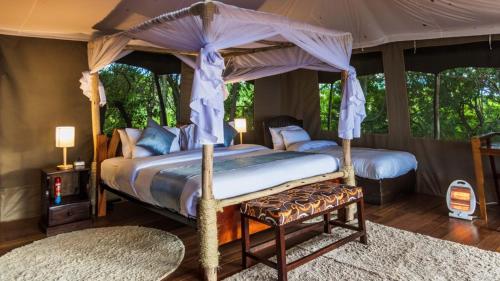 a bedroom with a canopy bed with a bench and a rug at Maasai home village in Sekenani