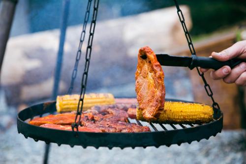 une personne cuisine de la viande et du maïs sur un grill dans l'établissement TrekkingCamp Himmelsterrassen, à Bad Peterstal-Griesbach