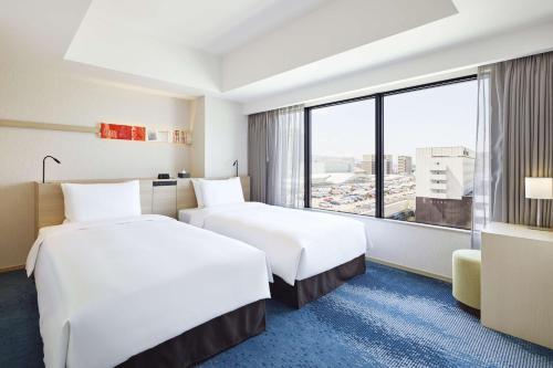 two beds in a hotel room with a large window at Hyatt House Kanazawa in Kanazawa