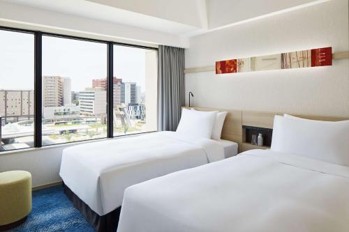 two beds in a hotel room with a large window at Hyatt House Kanazawa in Kanazawa