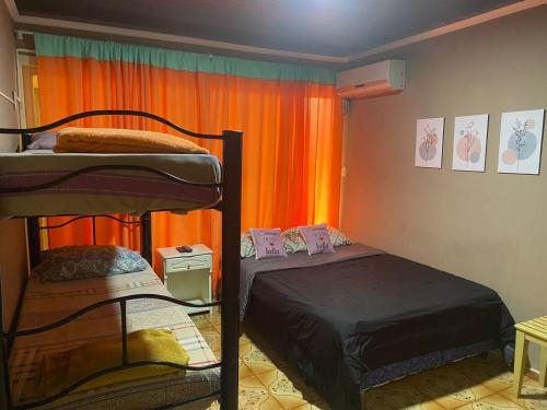 um quarto com 2 beliches e uma cortina laranja em Guembe al Rio Hostel em Puerto Iguazú