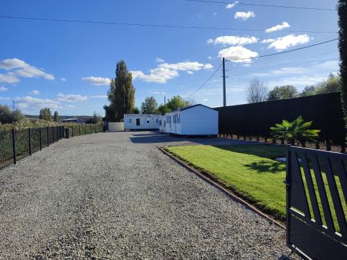 a gravel driveway with a fence and a white building at Mobil-home Côté Mur in Holque