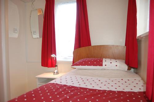 a bedroom with a bed with red curtains and a window at Wulfrun in Tywyn