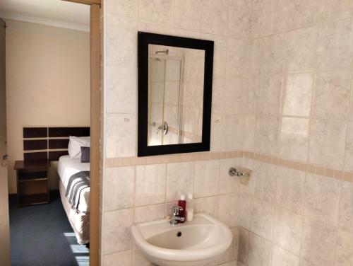 een badkamer met een wastafel, een spiegel en een bed bij Turquoise View Guesthouse in Middelburg