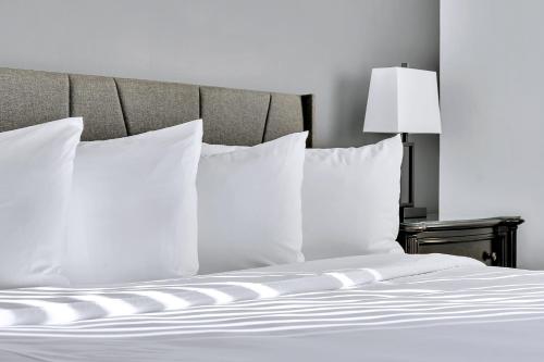a bed with white pillows and a table with a lamp at The Inn of Lake George in Lake George