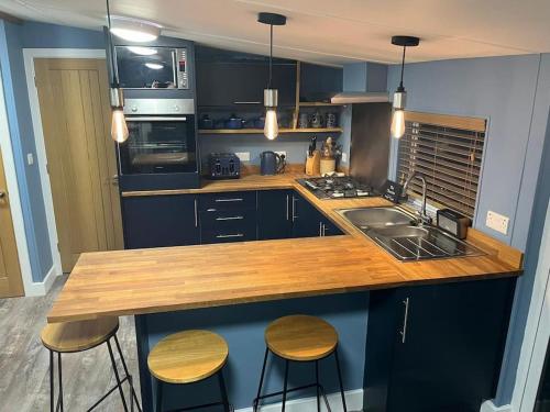 a kitchen with a wooden counter top with two stools at 2 bedroom lodge - The Cherries (24) Caer beris holiday park in Builth Wells