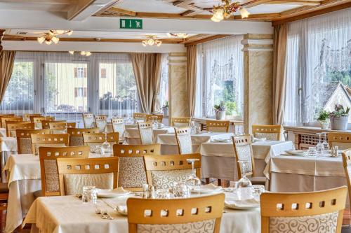 a restaurant with white tables and chairs and windows at Alpenresort Belvedere in Molveno