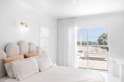 a white bedroom with a bed with a view of a patio at WhitsunStays - The Cyclades in Mackay