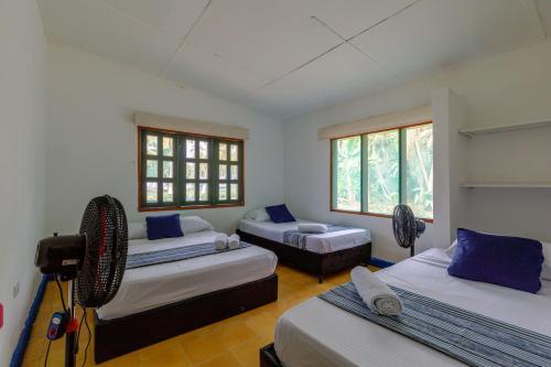 a room with three beds and a couch and windows at CASA DE CAMPO CASTILLETE dentro del PARQUE TAYRONA in Santa Marta