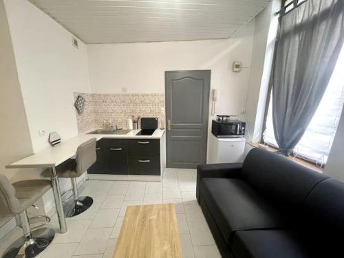 un salon avec un canapé noir et une cuisine dans l'établissement Studio confortable dans le centre de Douai, à Douai