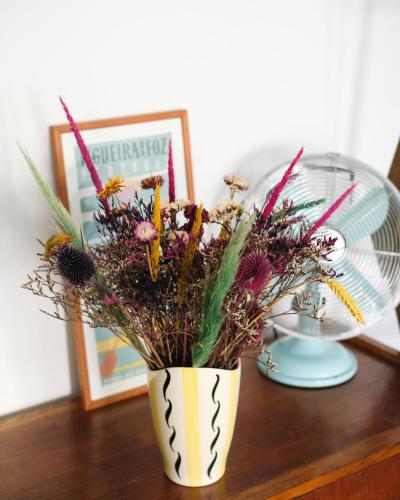 a vase filled with flowers on a table with a fan at Casa da Fonte - Vintage House and Rooftop in Figueira da Foz