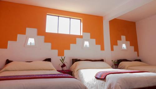 two beds in a room with an orange wall at Hostal Margarita Isla del Sol Norte comunidad Challapampa in Comunidad Challapampa