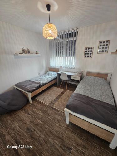 a bedroom with two beds and a table and a chandelier at Apartman Una in Zrenjanin