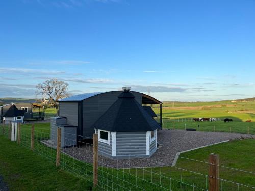 a building with a black roof next to a fence at Capledrae Farmstay Shepherds Huts in Cardenden