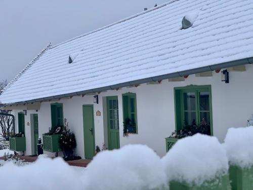 a white house with green doors and snow at Pannonhalma Várlak Vendégház in Pannonhalma