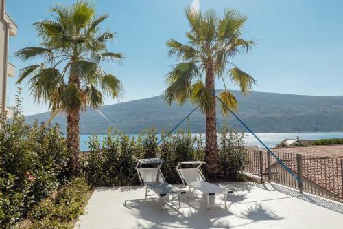 2 Stühle und Palmen auf einer Terrasse mit Meerblick in der Unterkunft Bella Vista Apartments in Baošići