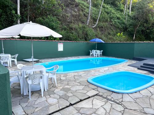 een zwembad met tafels en stoelen en een parasol bij Flats e Apartamentos Temporada Mar Brasil in Ubatuba
