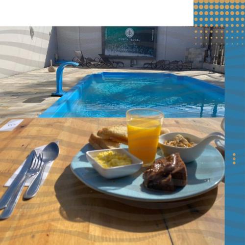 a plate of food and a glass of orange juice next to a swimming pool at Hostel Costa Terral in Matinhos