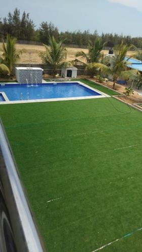 a swimming pool with green grass in front of it at Coastal Heaven Koovathur in Kūvattūr